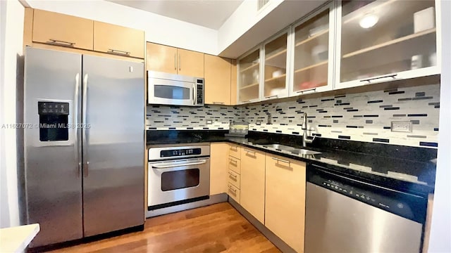 kitchen with sink, light hardwood / wood-style flooring, backsplash, dark stone counters, and appliances with stainless steel finishes