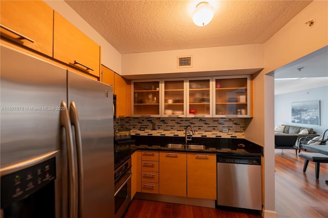 kitchen with sink, stainless steel appliances, dark wood-type flooring, dark stone countertops, and decorative backsplash