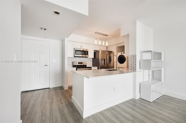 kitchen featuring appliances with stainless steel finishes, white cabinets, kitchen peninsula, light hardwood / wood-style floors, and decorative backsplash