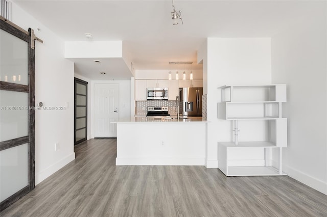 kitchen featuring light hardwood / wood-style floors, a barn door, backsplash, and stainless steel appliances