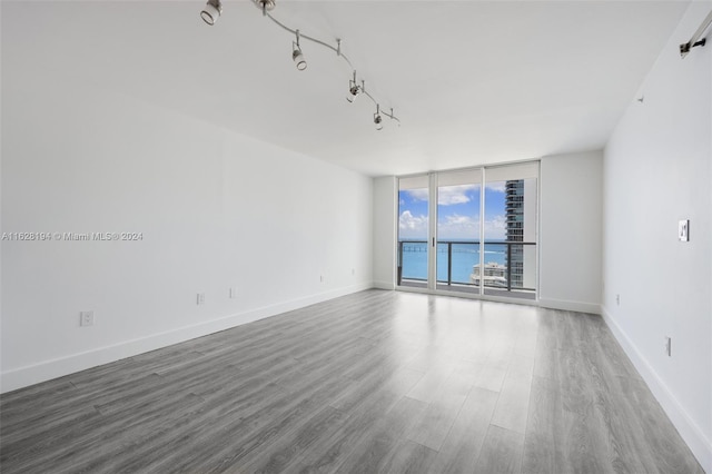 empty room featuring a water view, rail lighting, expansive windows, and hardwood / wood-style floors