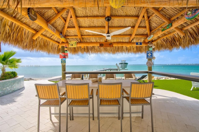 view of patio with ceiling fan, a gazebo, a water view, a beach view, and a bar