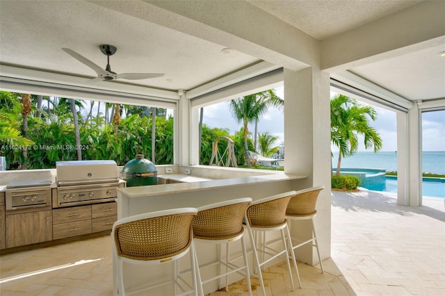 view of patio / terrace with an outdoor kitchen, area for grilling, an outdoor bar, ceiling fan, and a water view