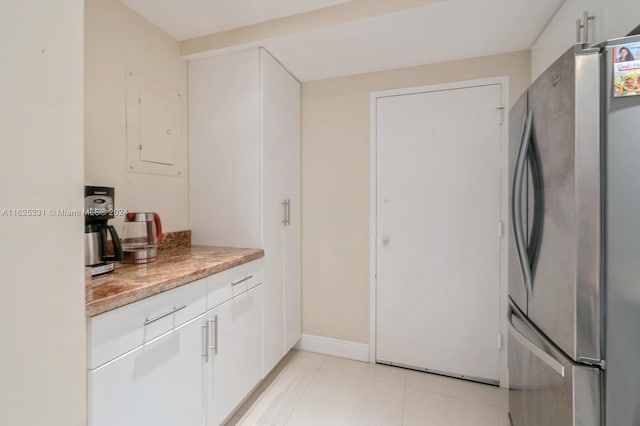 kitchen with light tile patterned floors, electric panel, stainless steel refrigerator, and white cabinets