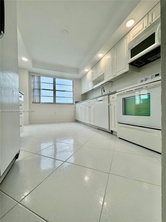 kitchen with white cabinets, a raised ceiling, light tile patterned floors, and white appliances