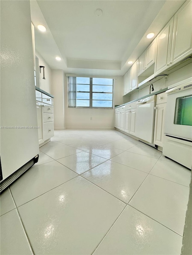 kitchen with light tile patterned flooring, a tray ceiling, white appliances, and white cabinetry