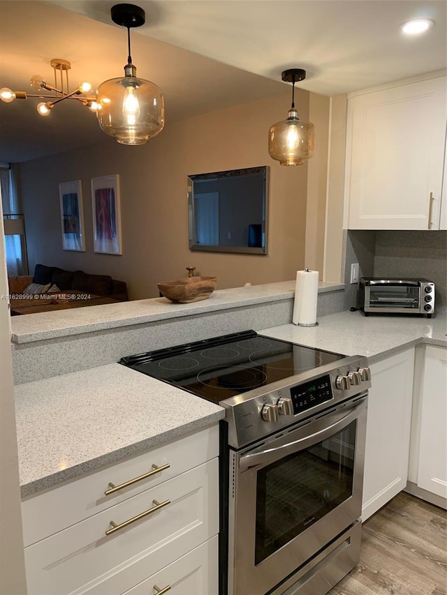 kitchen with stainless steel electric range, pendant lighting, light stone counters, light wood-type flooring, and white cabinetry