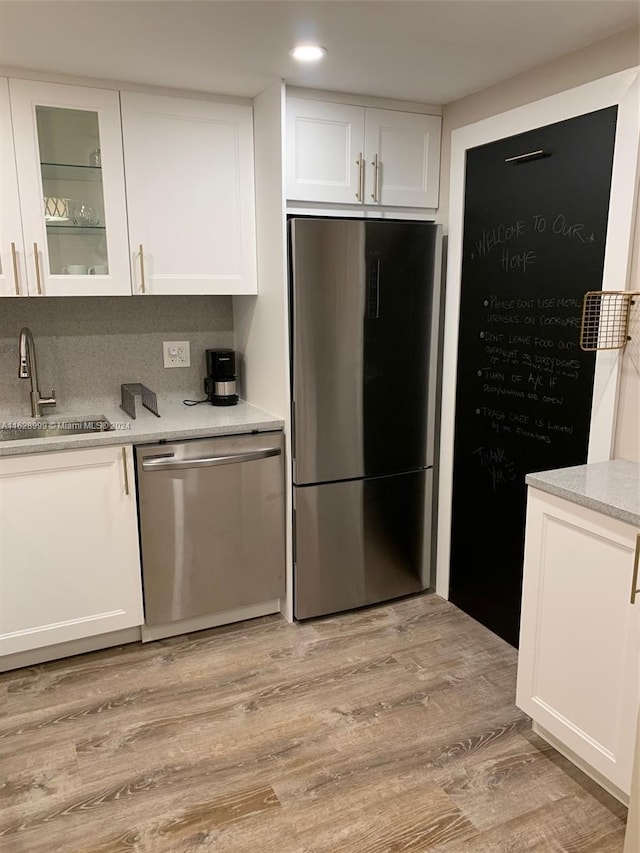 kitchen with light wood-type flooring, white cabinets, stainless steel appliances, decorative backsplash, and sink