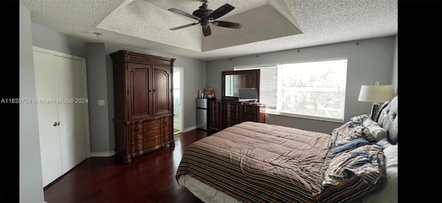 bedroom with ceiling fan, a textured ceiling, dark hardwood / wood-style flooring, and a raised ceiling