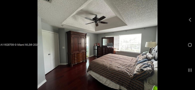 bedroom featuring a textured ceiling, ceiling fan, dark hardwood / wood-style floors, and a tray ceiling