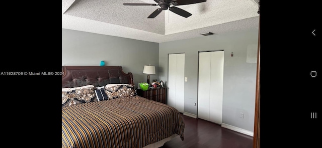 bedroom with ceiling fan, dark hardwood / wood-style floors, two closets, a tray ceiling, and a textured ceiling