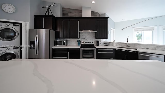 kitchen featuring backsplash, vaulted ceiling, appliances with stainless steel finishes, stacked washer / dryer, and sink