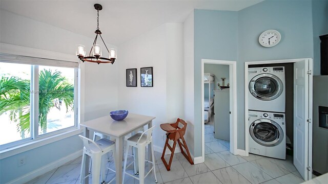 clothes washing area with plenty of natural light, stacked washer / drying machine, an inviting chandelier, and light tile patterned floors