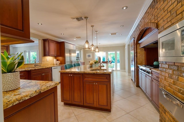 kitchen featuring sink, light stone counters, built in appliances, decorative light fixtures, and a center island with sink