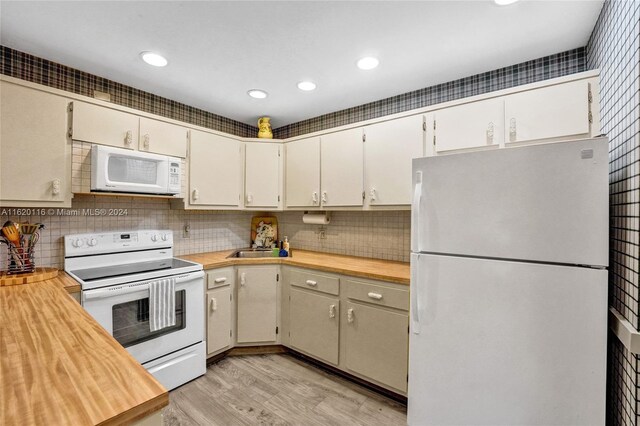 kitchen featuring tasteful backsplash, butcher block counters, sink, light wood-type flooring, and white appliances