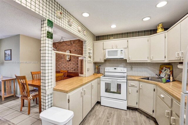 kitchen featuring light hardwood / wood-style flooring, white appliances, white cabinets, decorative backsplash, and brick wall