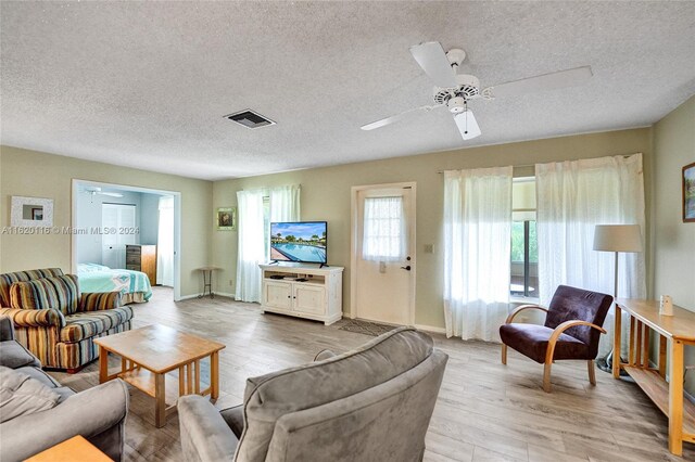 living room with a textured ceiling, ceiling fan, and light hardwood / wood-style flooring