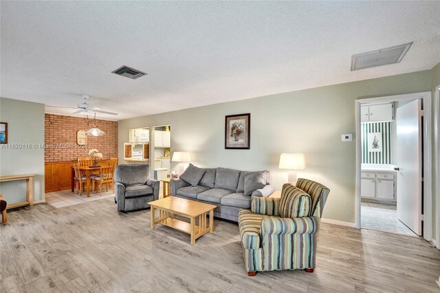 living room featuring light hardwood / wood-style floors, a textured ceiling, brick wall, and ceiling fan