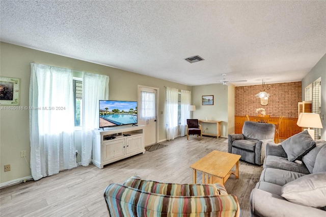 living room featuring ceiling fan, brick wall, a textured ceiling, and light hardwood / wood-style flooring