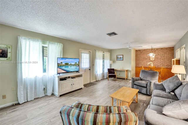 living room featuring ceiling fan, brick wall, a textured ceiling, and light wood-type flooring