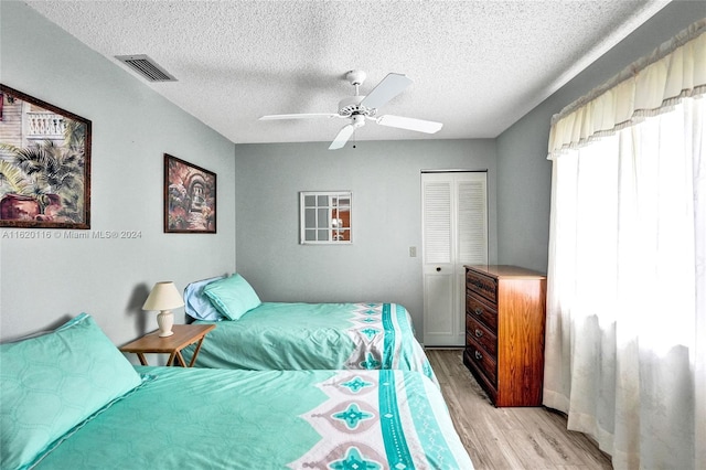 bedroom with a closet, ceiling fan, light hardwood / wood-style floors, and a textured ceiling