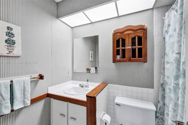 bathroom with vanity, toilet, and tile walls