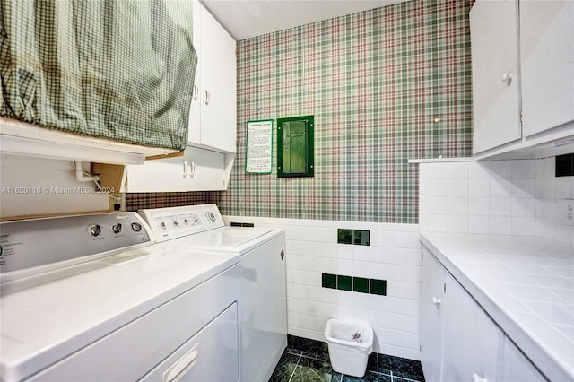 clothes washing area with separate washer and dryer, dark tile patterned floors, cabinets, and tile walls