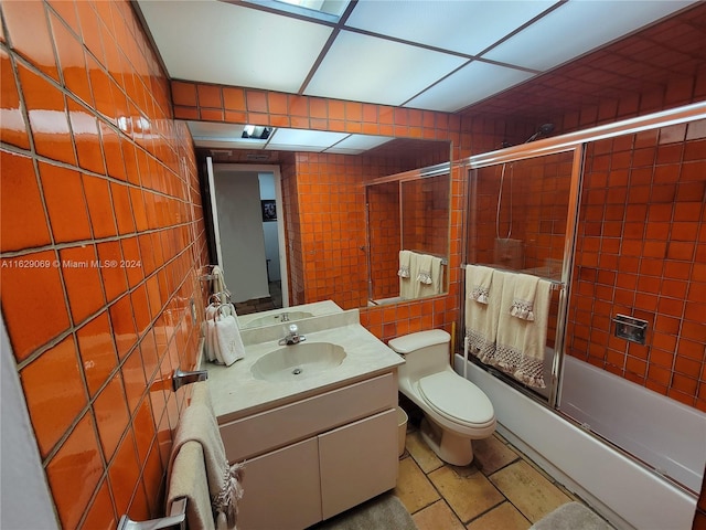 full bathroom featuring tile walls, shower / bath combination with glass door, vanity, and toilet