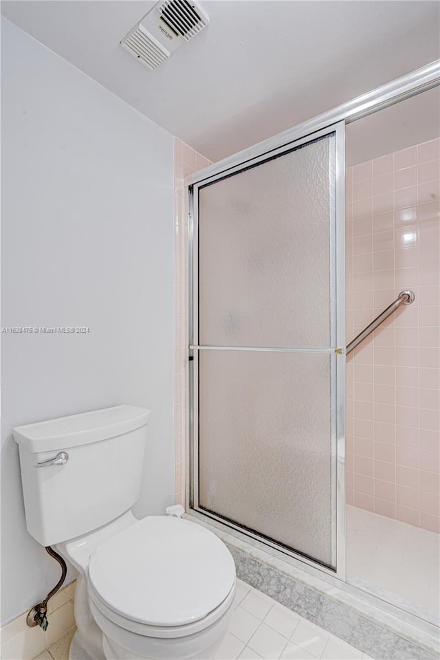 bathroom with tile patterned floors, toilet, and a shower with door