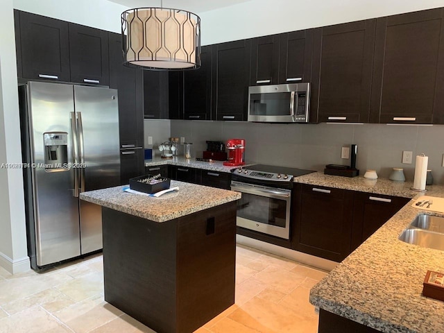 kitchen with stone tile floors, dark cabinets, a kitchen island, light stone countertops, and appliances with stainless steel finishes
