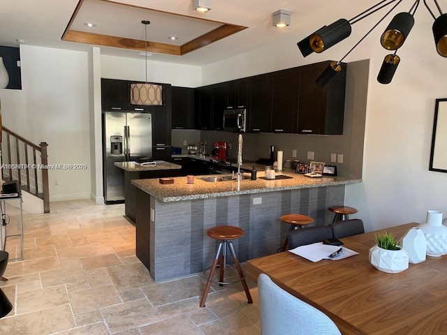 kitchen featuring kitchen peninsula, appliances with stainless steel finishes, a kitchen bar, a tray ceiling, and sink