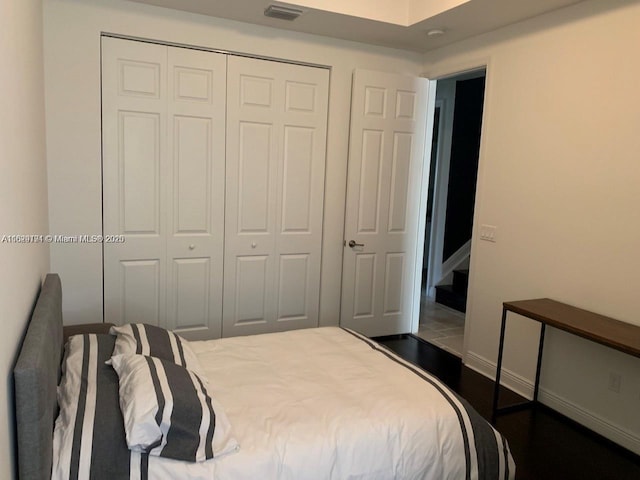 bedroom with baseboards, dark wood-type flooring, visible vents, and a closet