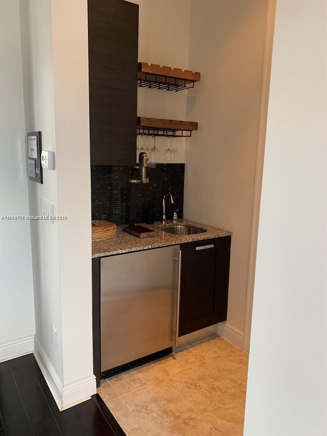 bar with baseboards, freestanding refrigerator, a sink, wet bar, and backsplash