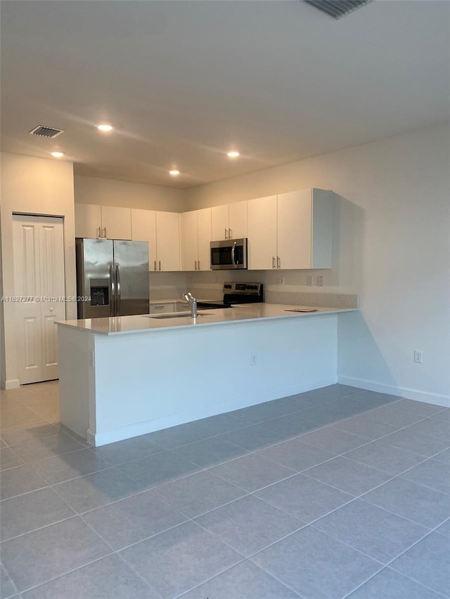 kitchen featuring light tile patterned floors, kitchen peninsula, white cabinets, stainless steel appliances, and sink