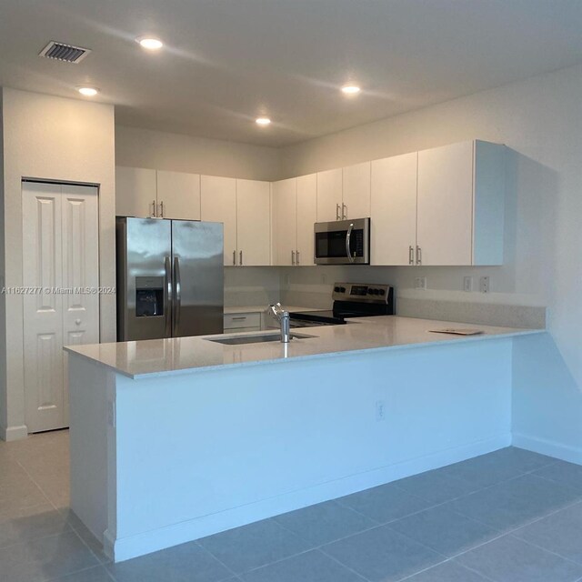 kitchen featuring sink, light tile patterned floors, appliances with stainless steel finishes, white cabinets, and kitchen peninsula