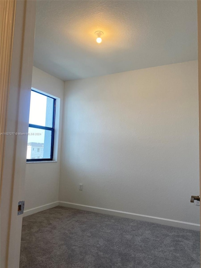 unfurnished room with a textured ceiling and dark colored carpet