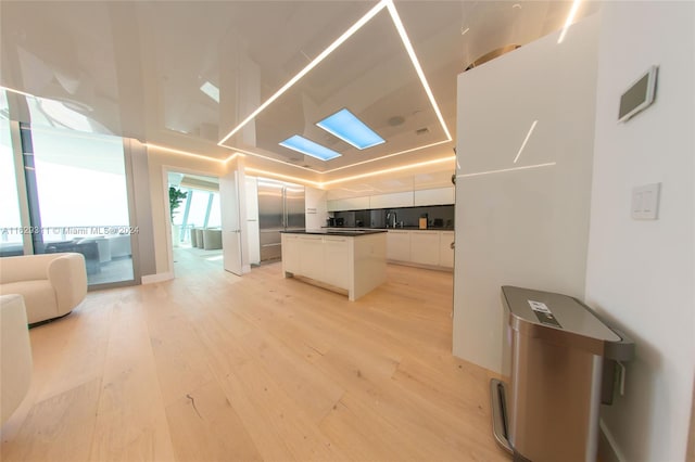 interior space with light hardwood / wood-style flooring, a center island, sink, and white cabinetry