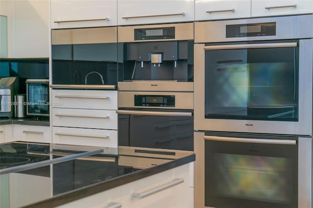 kitchen with dark stone counters, white cabinetry, and stainless steel double oven