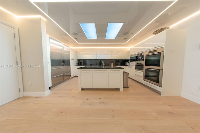 kitchen with stainless steel double oven, light wood-type flooring, white cabinetry, and a center island