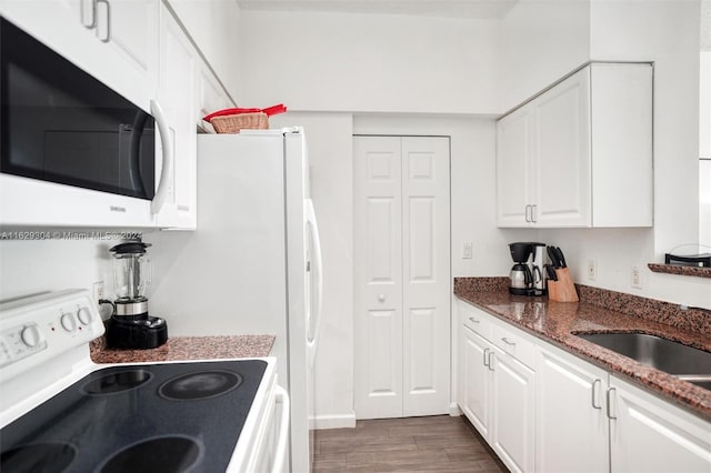 kitchen featuring white appliances, dark wood finished floors, dark stone counters, a sink, and white cabinets