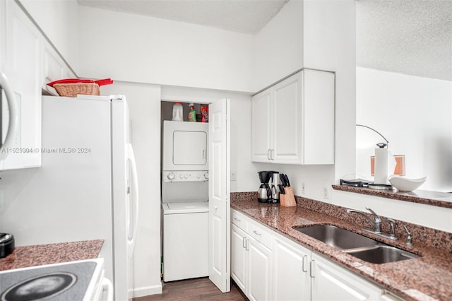 kitchen featuring dark wood-style floors, stacked washing maching and dryer, a sink, white cabinets, and a textured ceiling