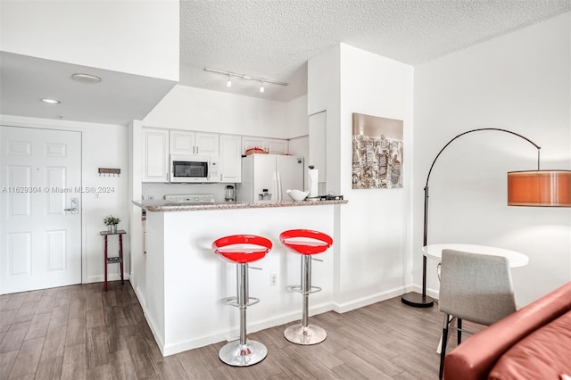 kitchen featuring a breakfast bar, wood finished floors, white cabinets, white appliances, and a textured ceiling
