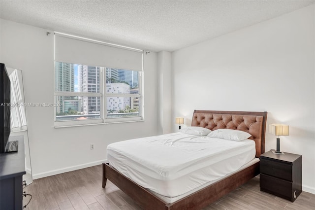 bedroom with wood finished floors, baseboards, and a textured ceiling