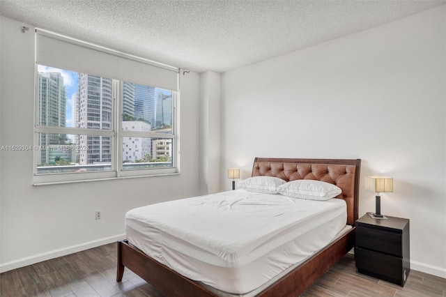 bedroom with a view of city, a textured ceiling, baseboards, and wood finished floors