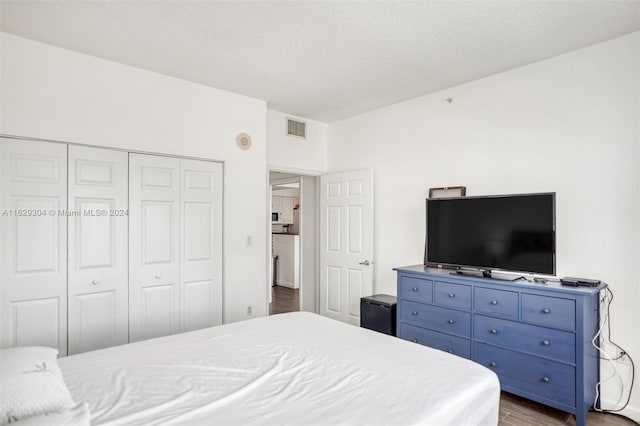 bedroom featuring dark wood-style floors, visible vents, a textured ceiling, and a closet