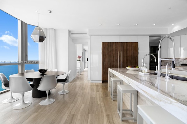 kitchen with tasteful backsplash, hanging light fixtures, white cabinets, light hardwood / wood-style floors, and light stone countertops