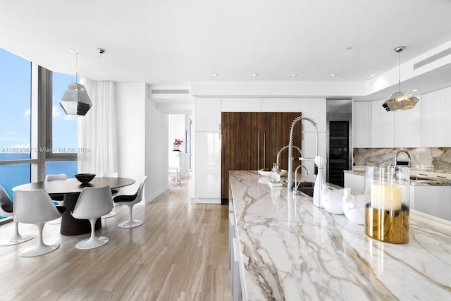 kitchen with decorative backsplash, light hardwood / wood-style flooring, pendant lighting, white cabinets, and light stone countertops