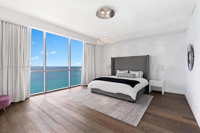 bedroom featuring dark wood-type flooring, a water view, an inviting chandelier, and access to exterior