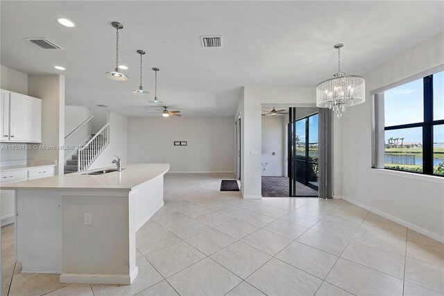 kitchen featuring ceiling fan with notable chandelier, a water view, light tile patterned floors, and an island with sink