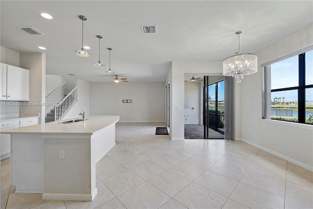 kitchen with sink, a water view, white cabinetry, an island with sink, and ceiling fan with notable chandelier